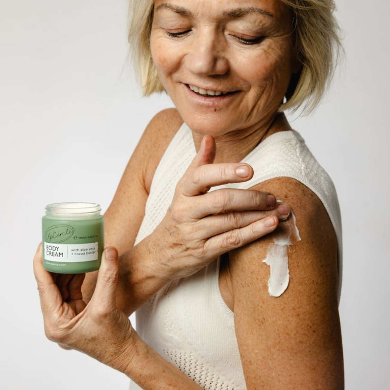 Woman applying body cream to her arm with a jar of cream in her hand.