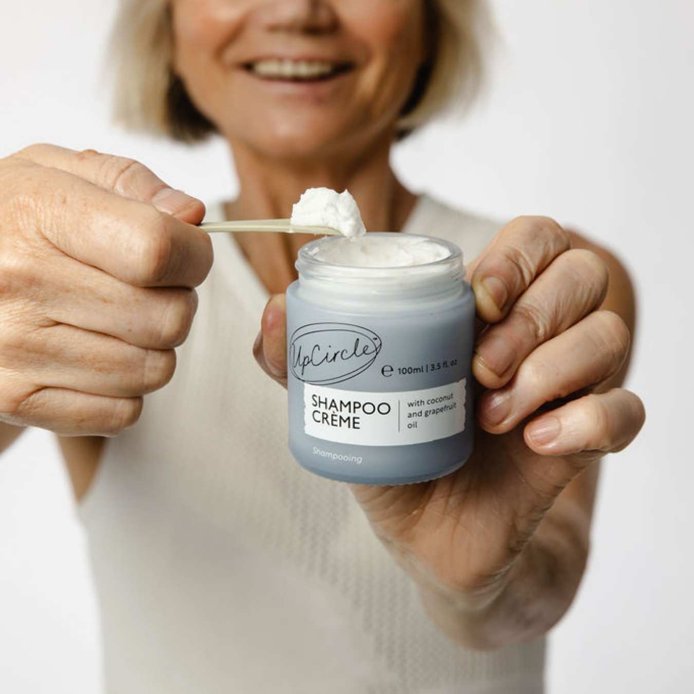 Person holding a jar of UpCircle Shampoo Crème with a spoonful of product.