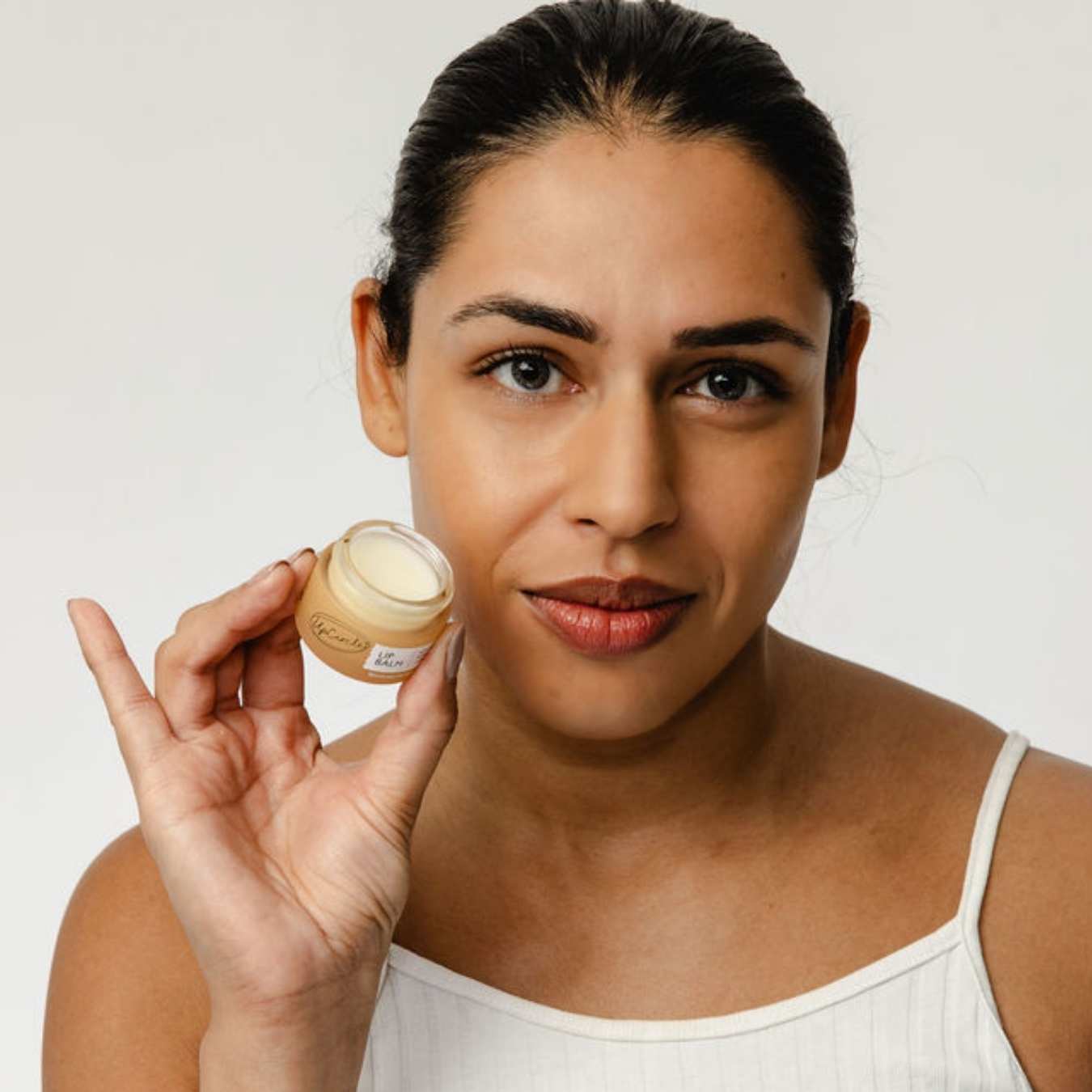 Woman holding a small jar of lip balm against a plain background