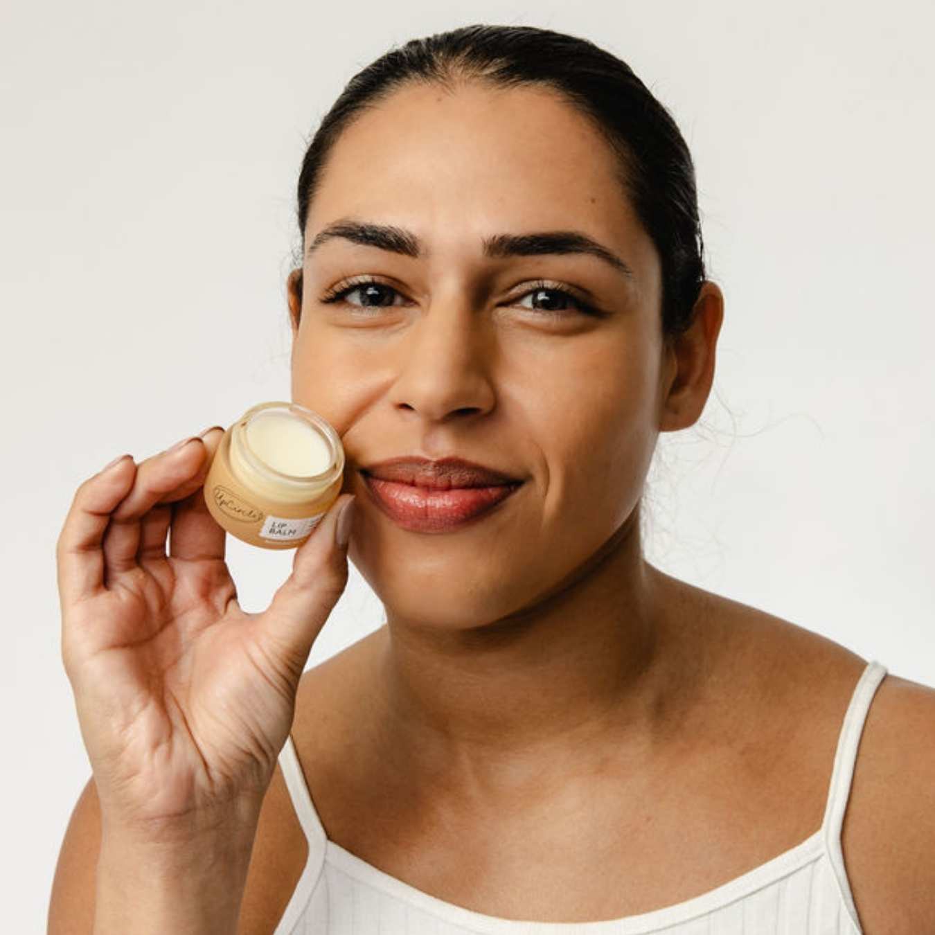 Woman holding a jar of lip balm against a white background