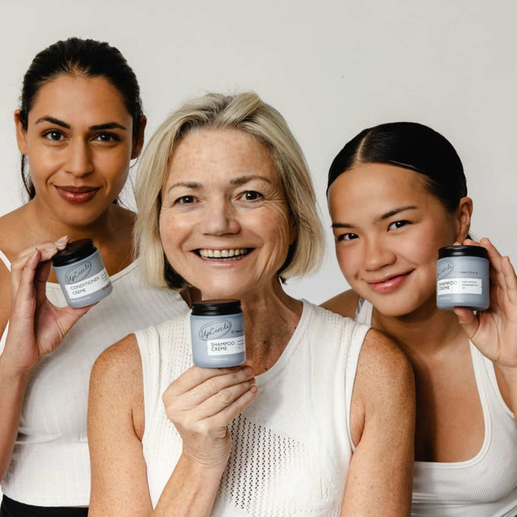 Three women holding skincare products against a plain background