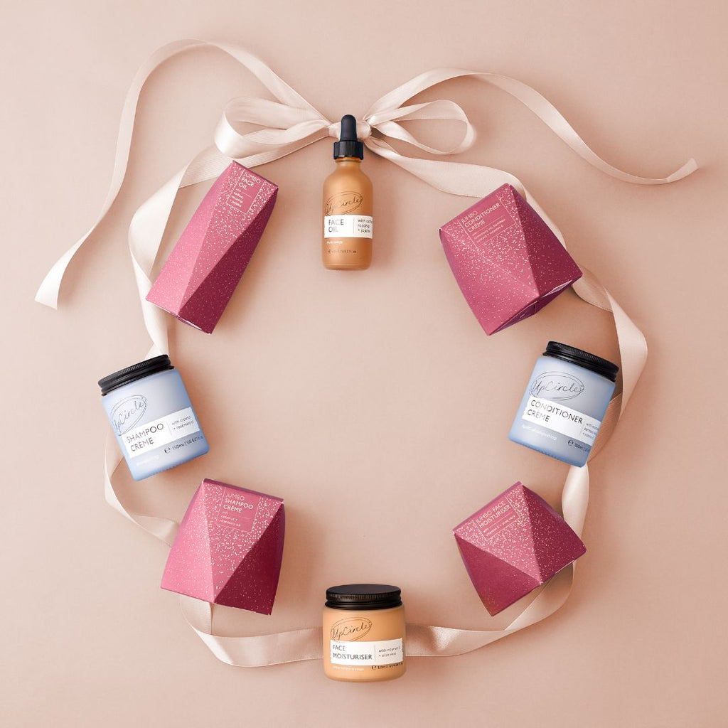 Cosmetic products including bottles and boxes arranged on a pink background with ribbons.