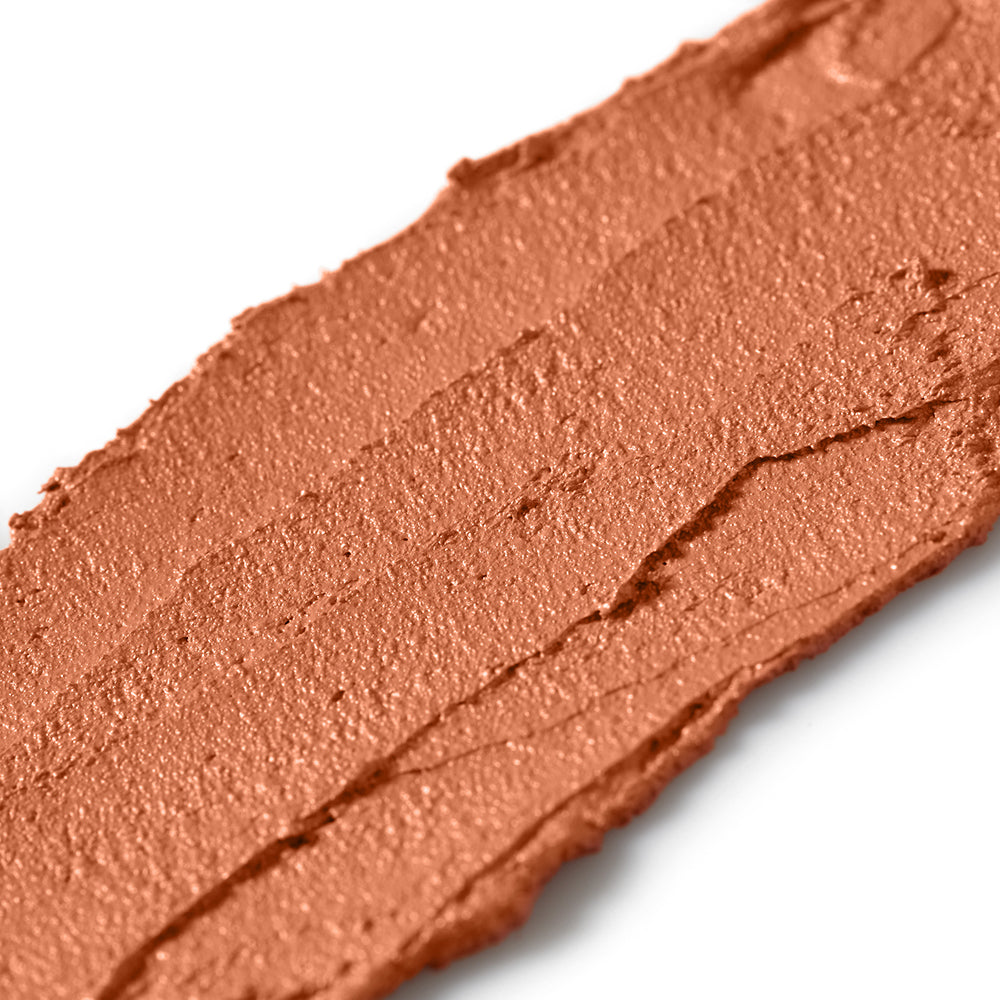 Close-up of a swatch of peachy orange makeup cream on a white background