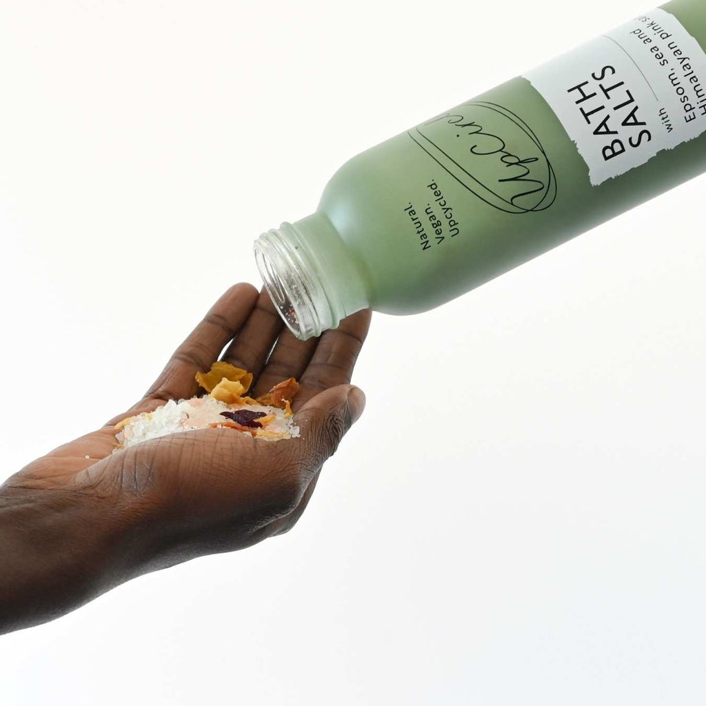 Bottle of bath salts being poured onto a hand with a white background