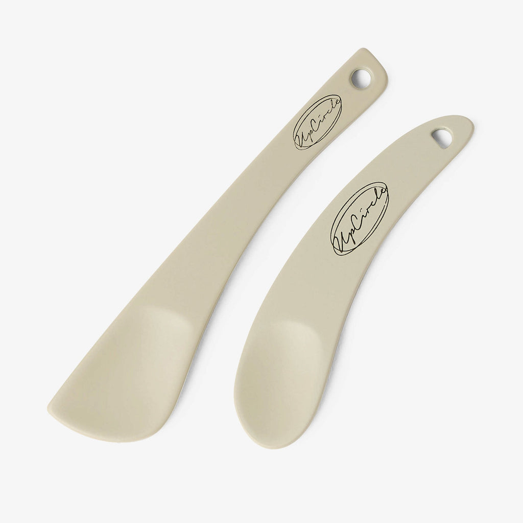 Two beige cosmetic spatulas with a brand logo on a white background