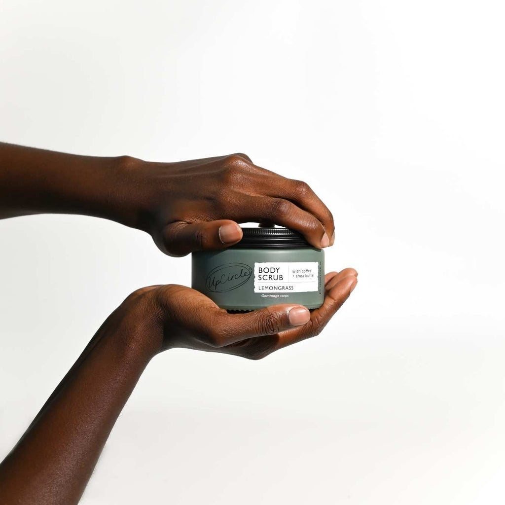 Two hands holding a jar of body scrub with a white background