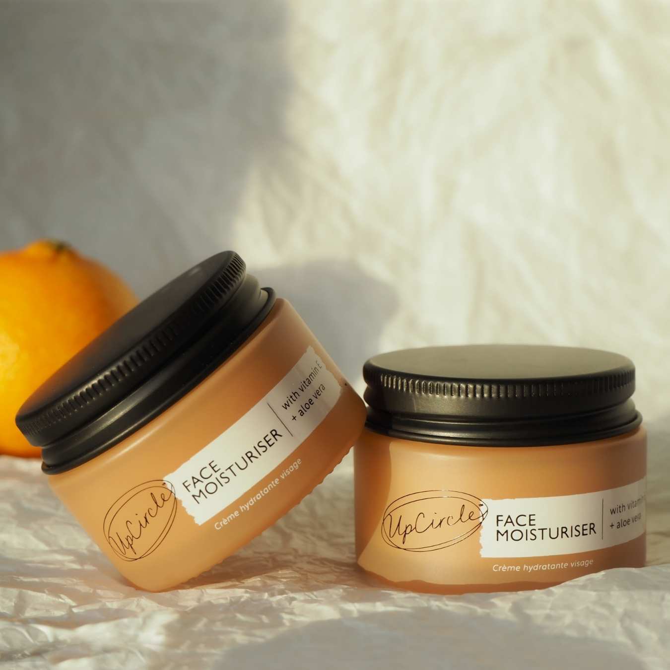 Two jars of UpCircle Face Moisturiser on a soft fabric background