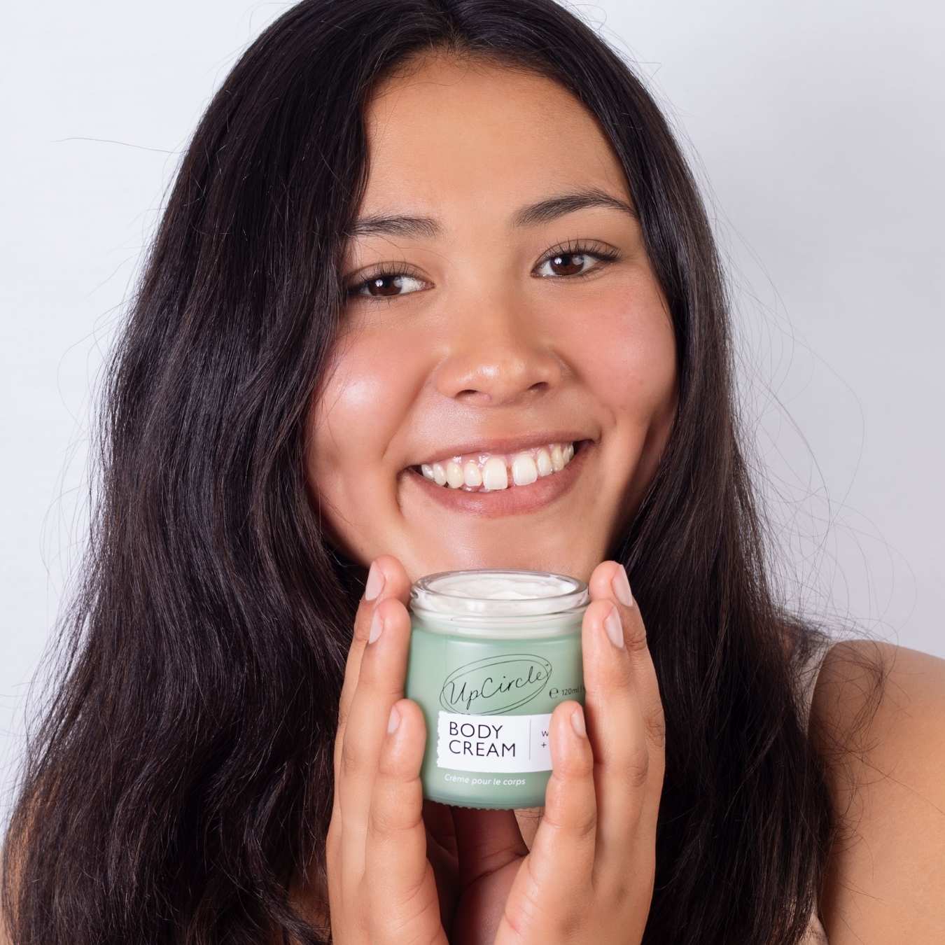 Woman holding a jar of body cream with a plain background