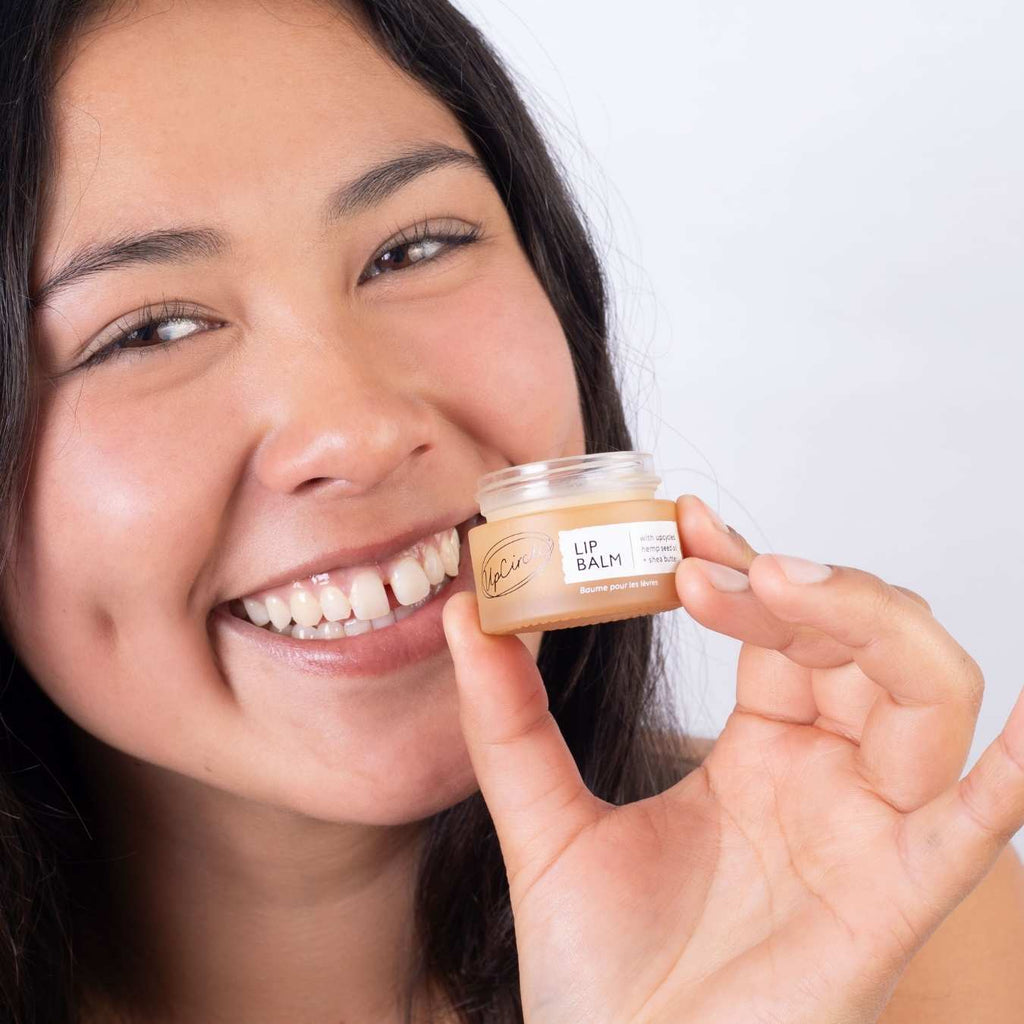 Woman holding a lip balm container with a plain background