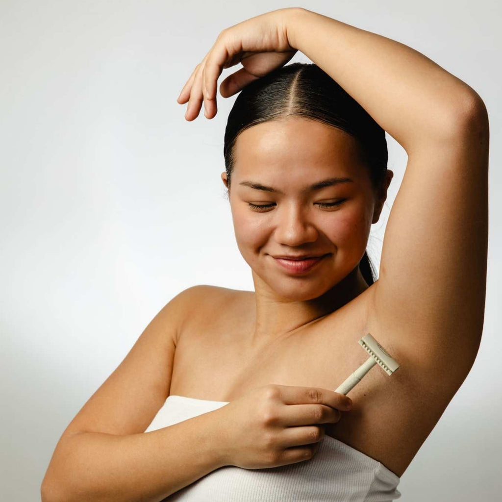 Woman shaving her arm with a razor against a plain background