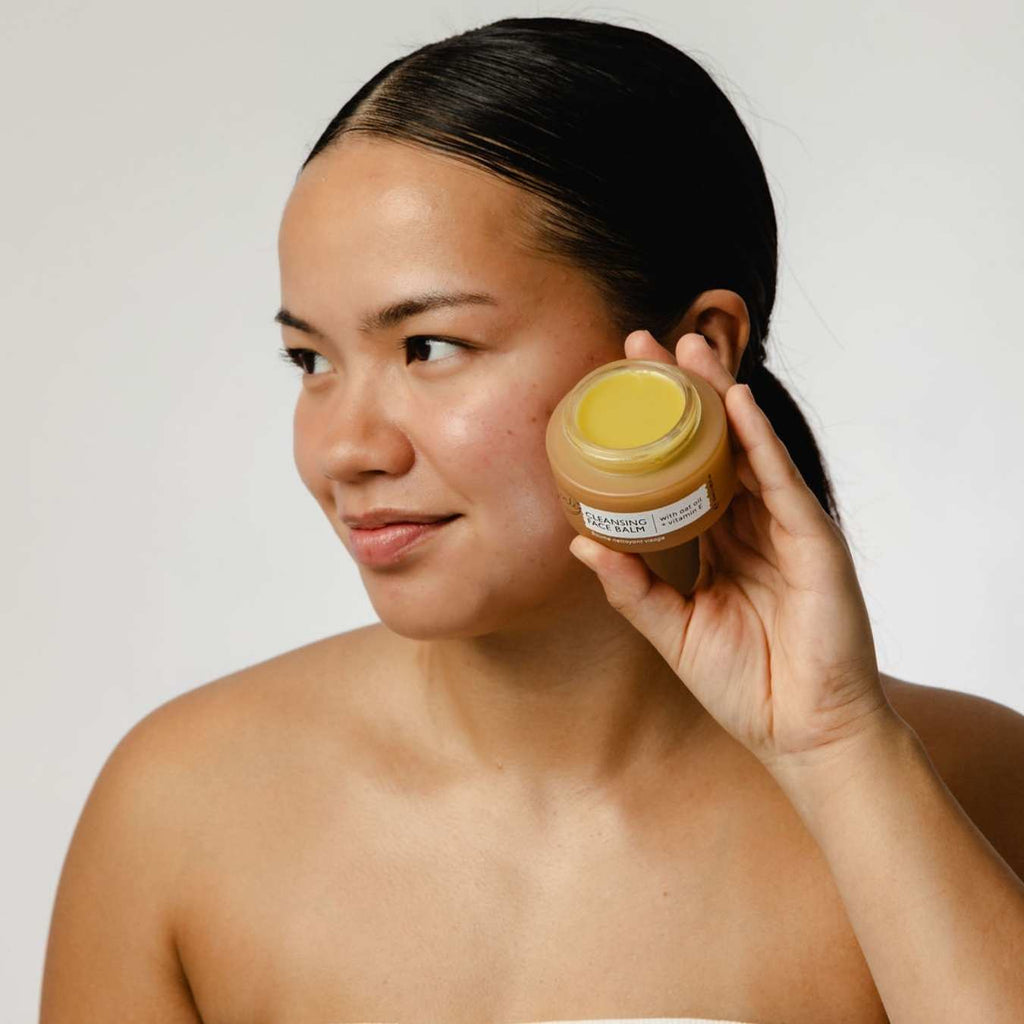 Woman holding a jar of cream next to her face against a plain background