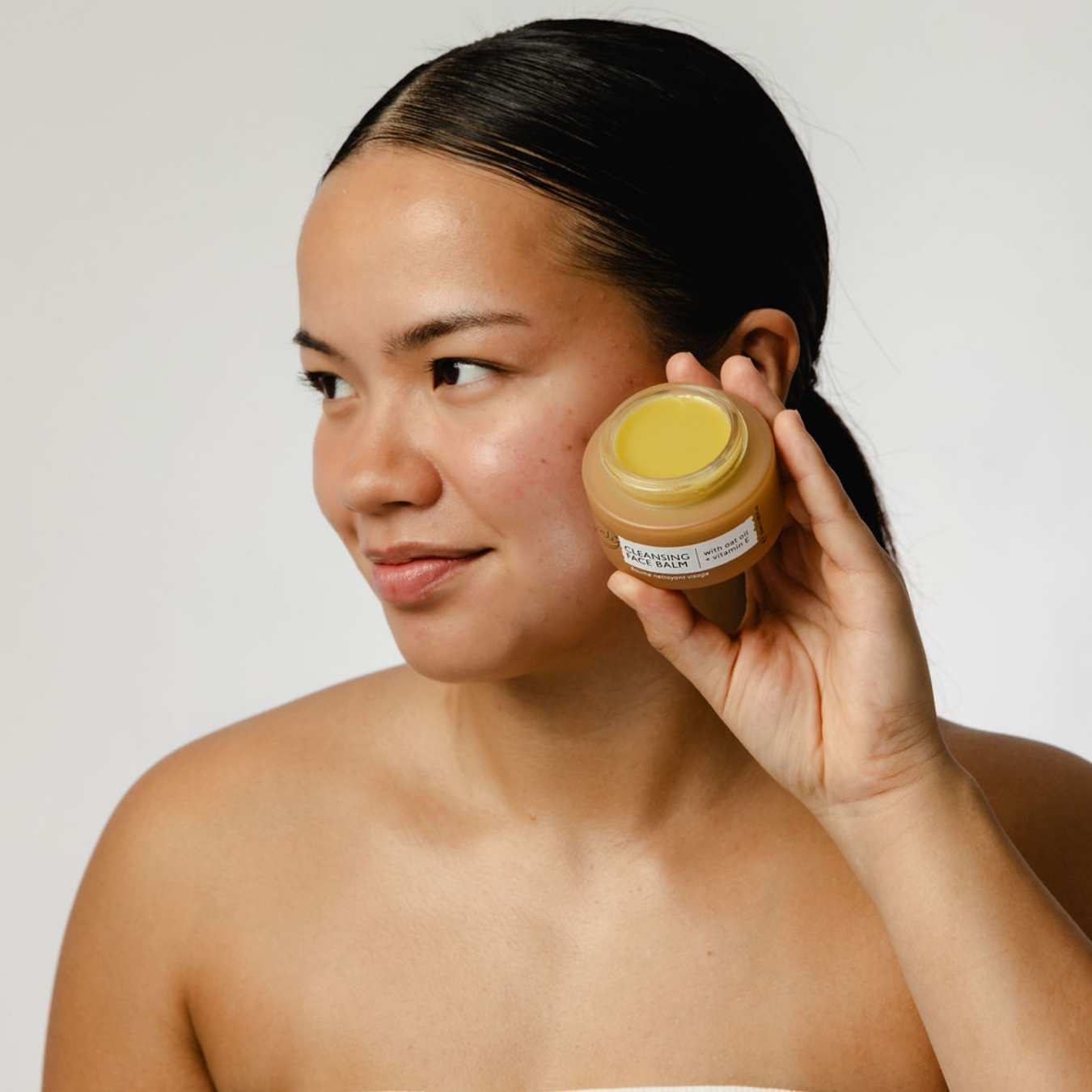 Woman holding a jar of cream next to her face against a plain background