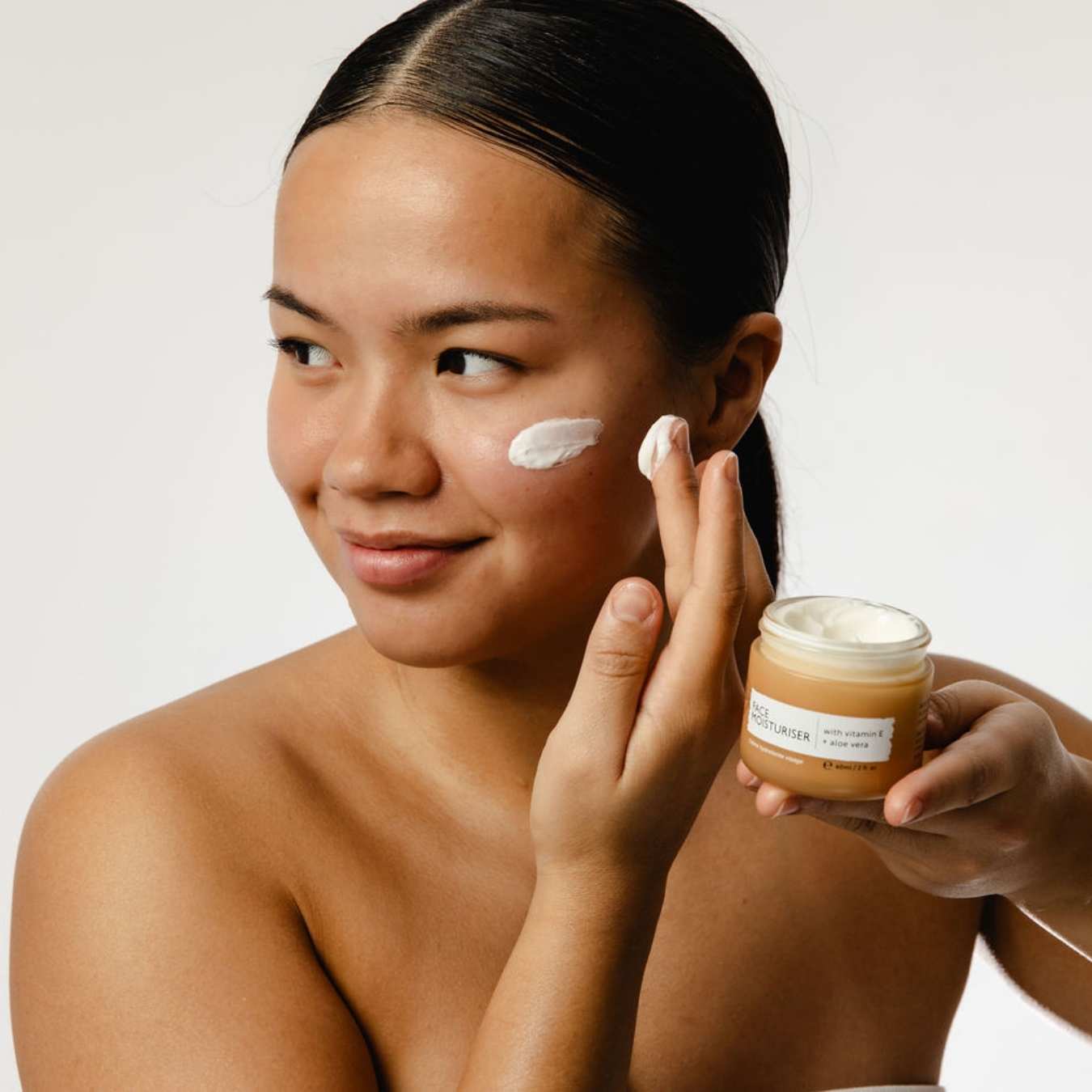 Woman applying cream to her face with a jar of cream in her hand.