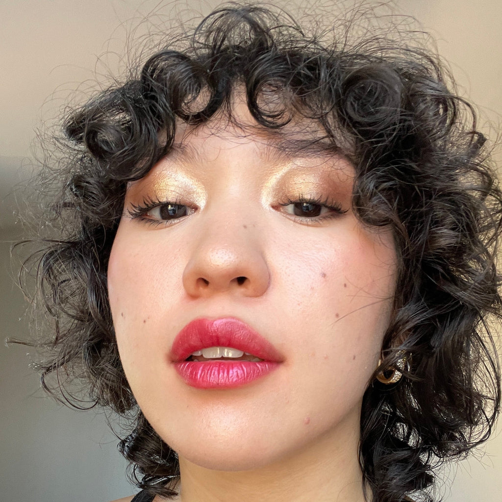 Close-up of a person with curly hair and pink lipstick against a neutral background