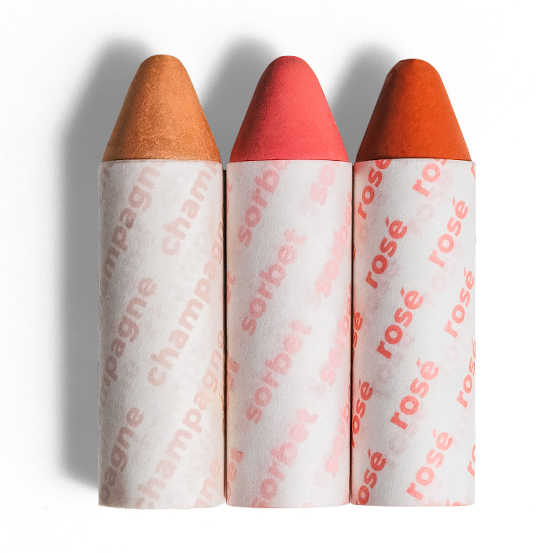 Three makeup crayons with branded paper wrappers on a white background