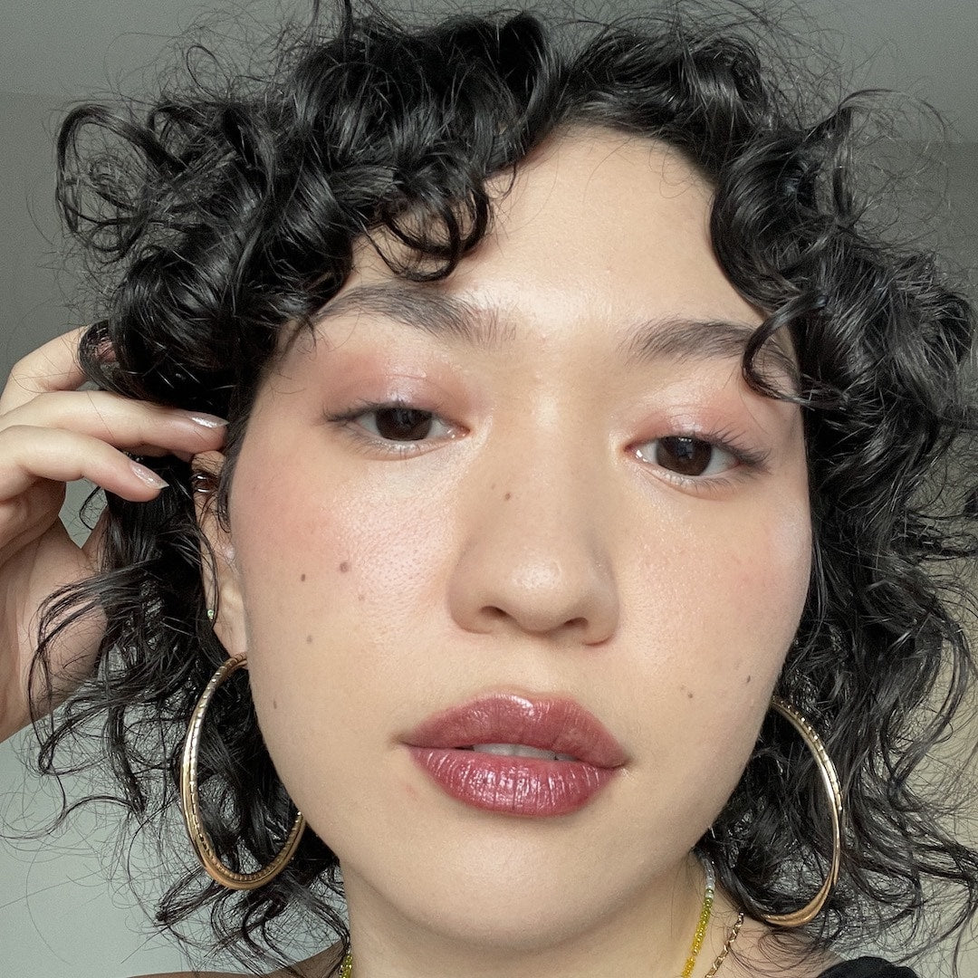 Close-up of a person with curly hair wearing makeup against a neutral background