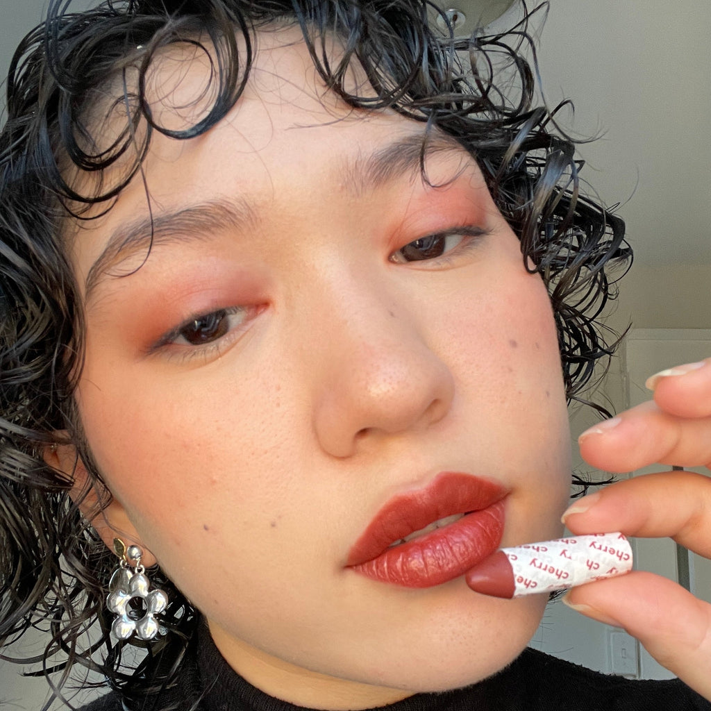 Person wearing makeup holding a 'cherry' lip crayon with a neutral background