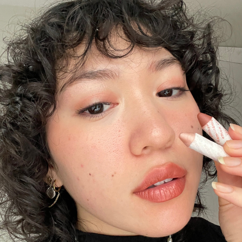 Person holding a lip crayon near their lips with a neutral background