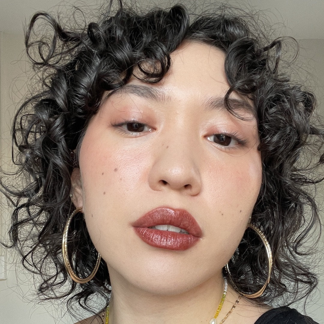Close-up of a person with curly hair wearing gold hoop earrings and red lipstick.