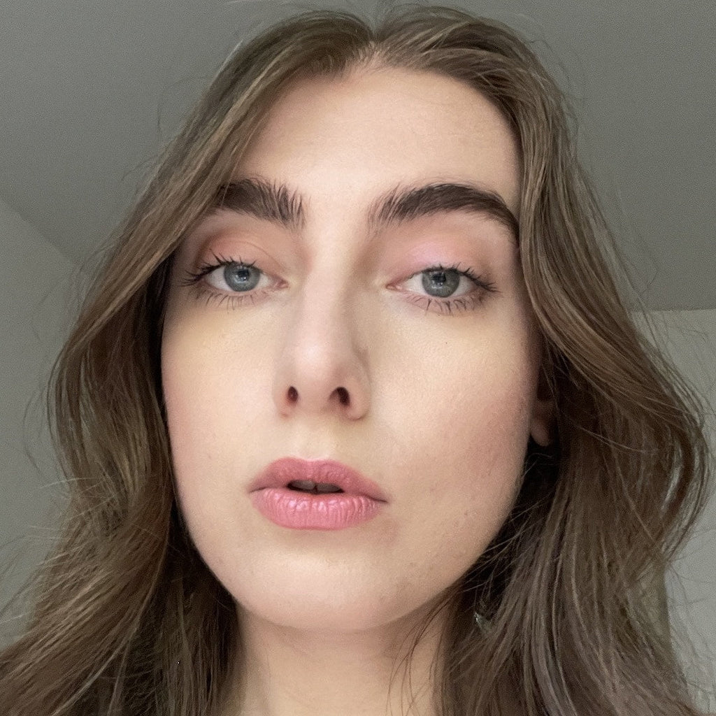 Close-up of a person with long, wavy hair wearing makeup against a neutral background