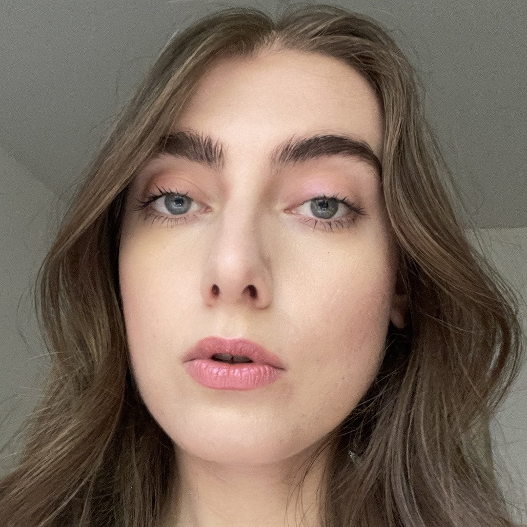 Close-up of a person with long, wavy hair wearing makeup against a neutral background