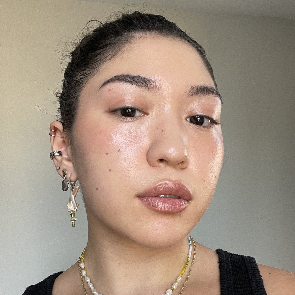 Close-up of a person with earrings and a necklace against a neutral background