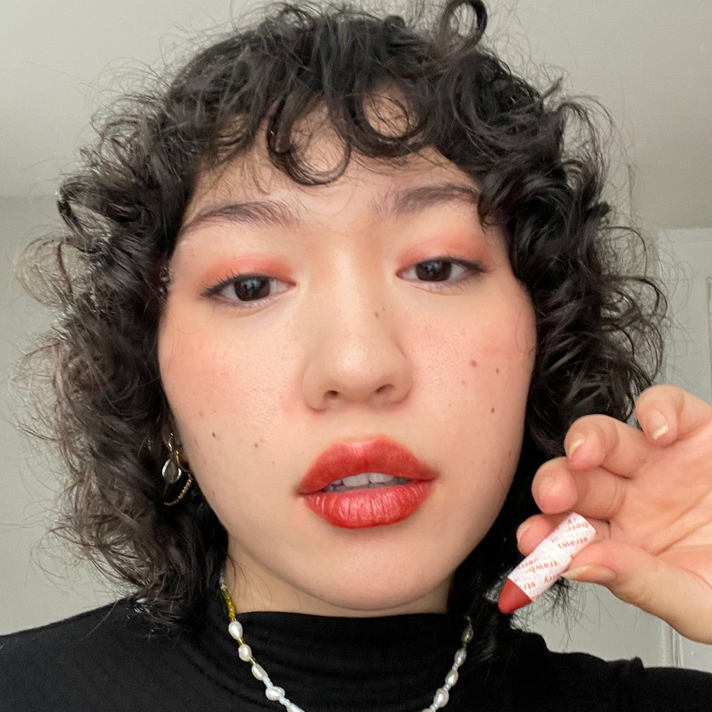 Person wearing makeup holding a red lip crayon with a neutral background