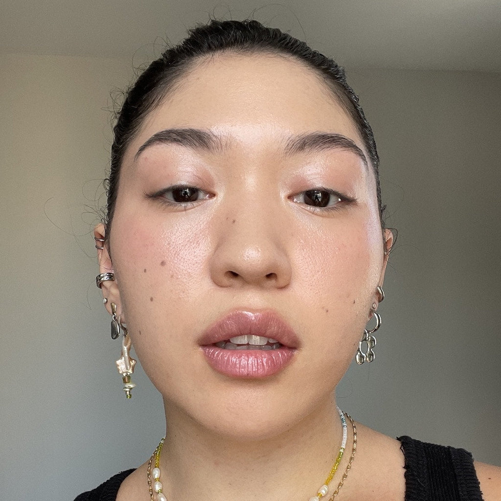 Close-up of a person wearing makeup with earrings and a necklace against a neutral background