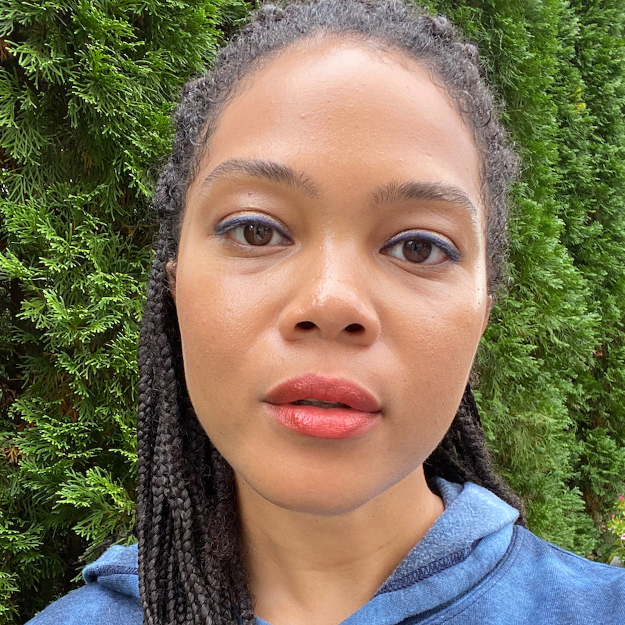 Woman with braided hair wearing makeup in front of green foliage