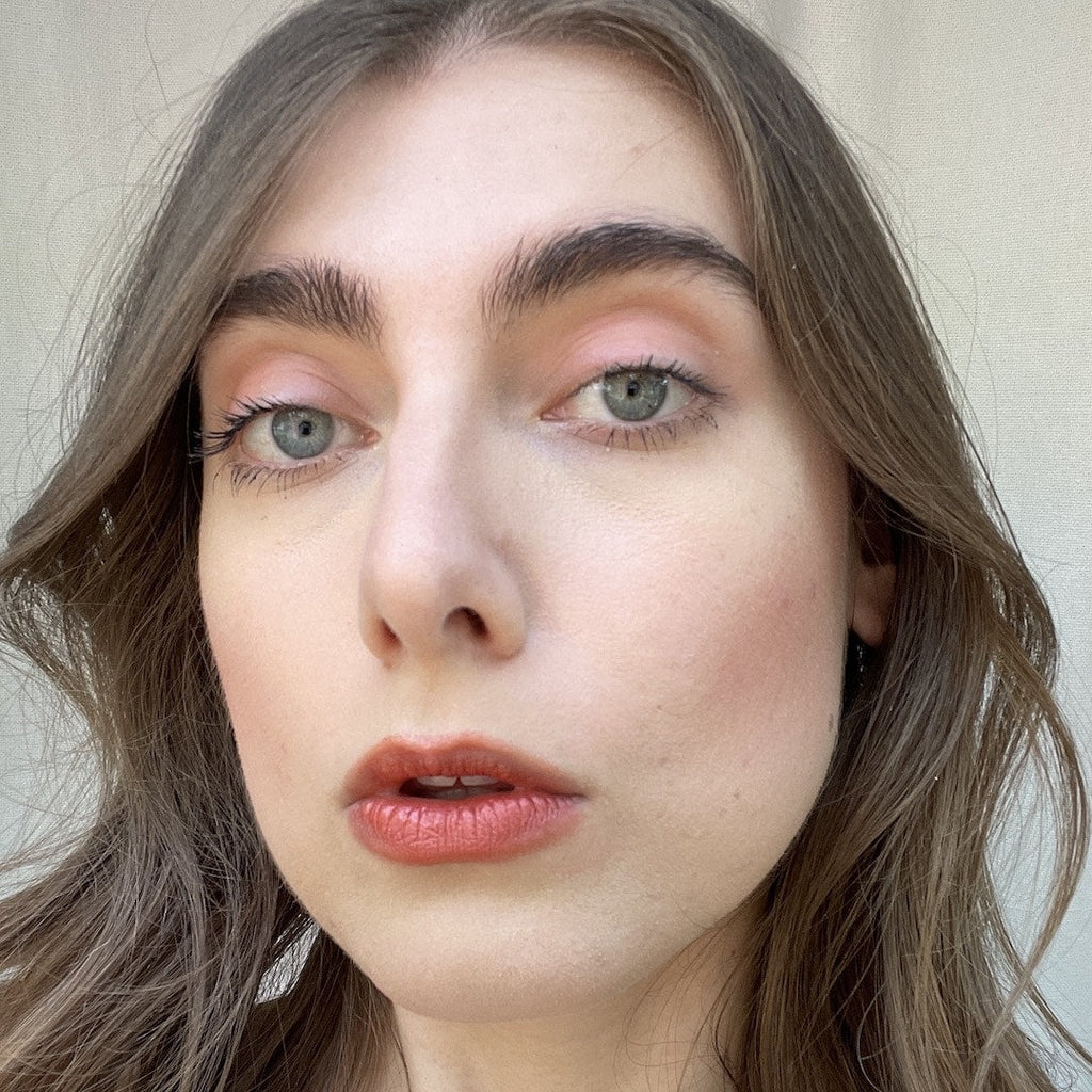 Close-up of a person with light makeup against a neutral background