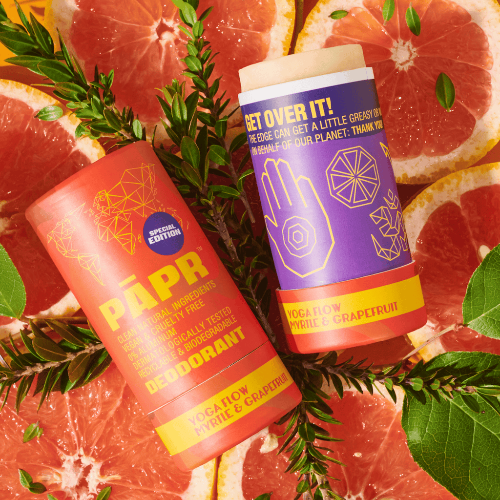 Two deodorant sticks with colorful labels on a background of grapefruit slices and green leaves.