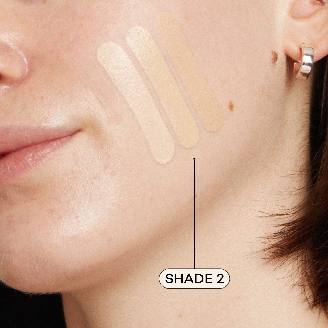 Close-up of a woman's face with foundation swatches on her cheek, labeled 'Shade 2'.