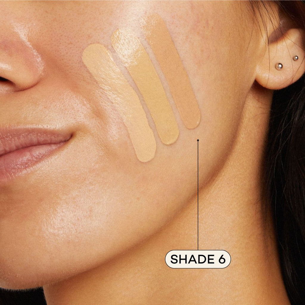 Close-up of a woman's face with foundation swatches on her cheek, labeled 'Shade 6'.