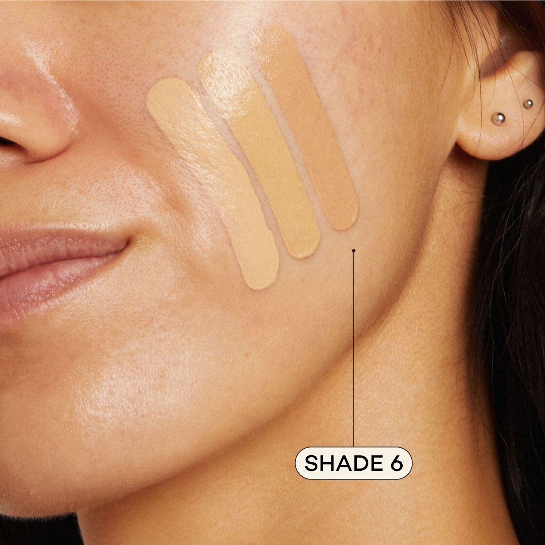 Close-up of a woman's face with foundation swatches on her cheek, labeled 'Shade 6'.