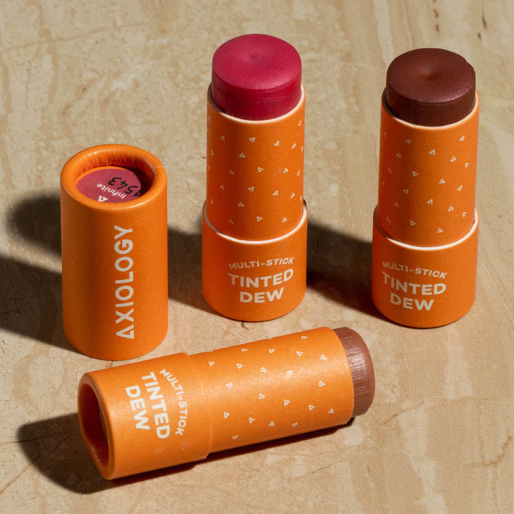 Multiple orange Axiology tinted dew multi-sticks on a beige background