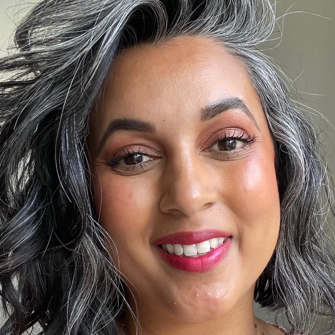 Close-up of a person with gray hair and pink lipstick against a neutral background