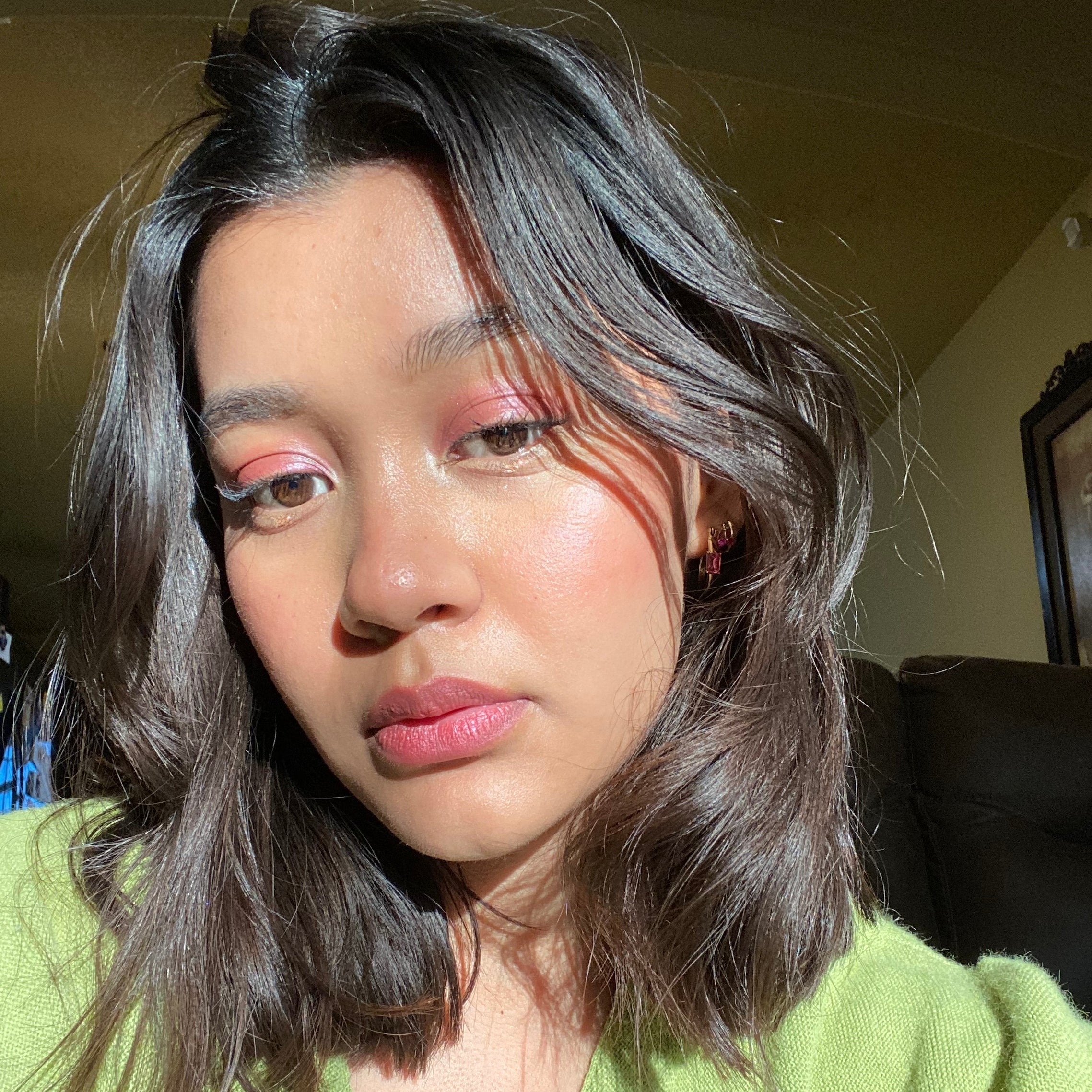 Person with shiny hair and pink makeup wearing a green sweater indoors.