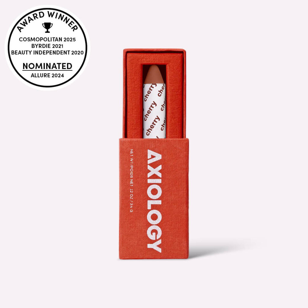 Axiology 'cherry' lip crayon in a red box with award badges on a white background