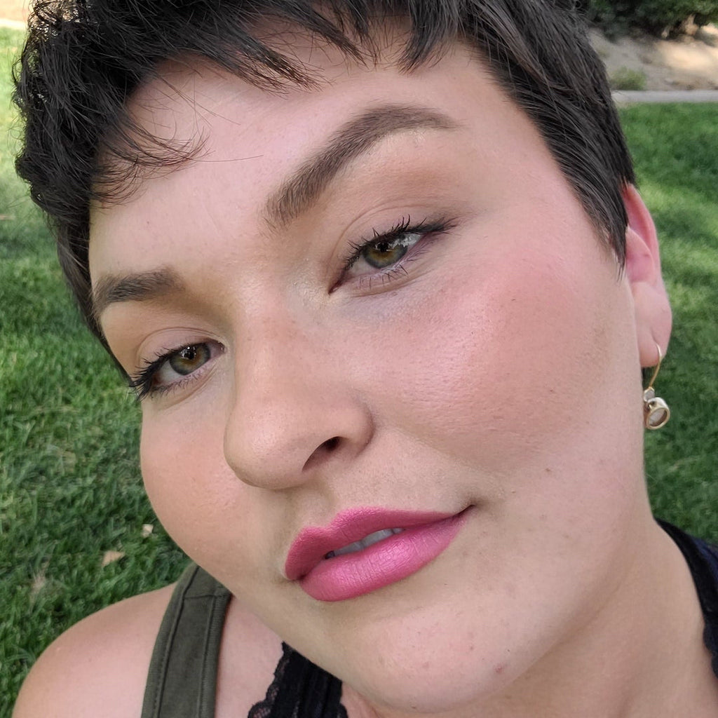Close-up of a person with short hair and pink lipstick against a grassy background