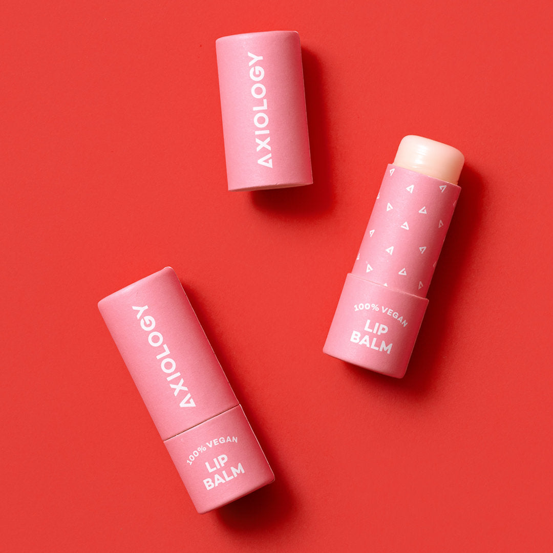Two pink lip balm tubes with 'Axiology' branding on a red background