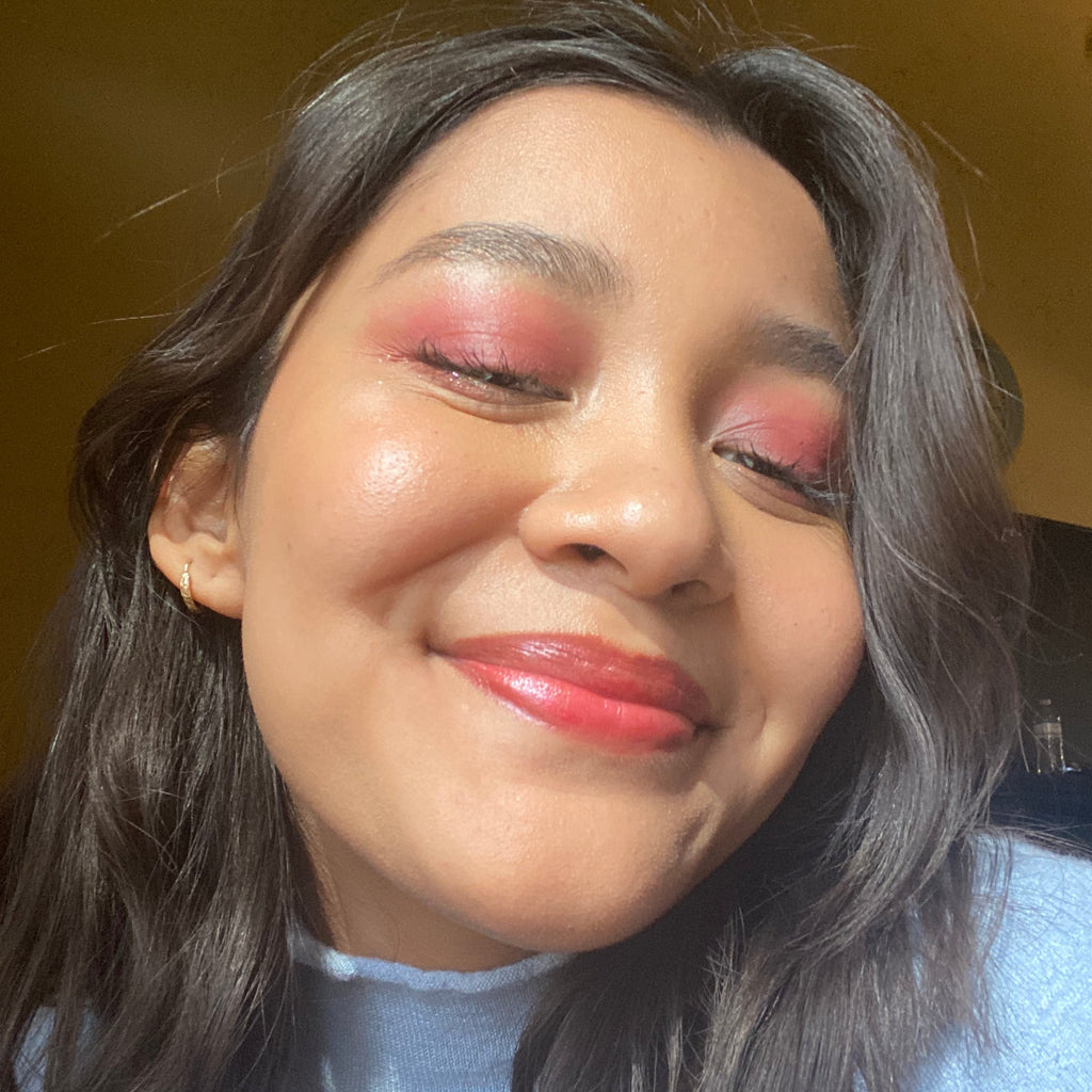 Close-up of a person with pink eyeshadow and red lipstick against a yellow background