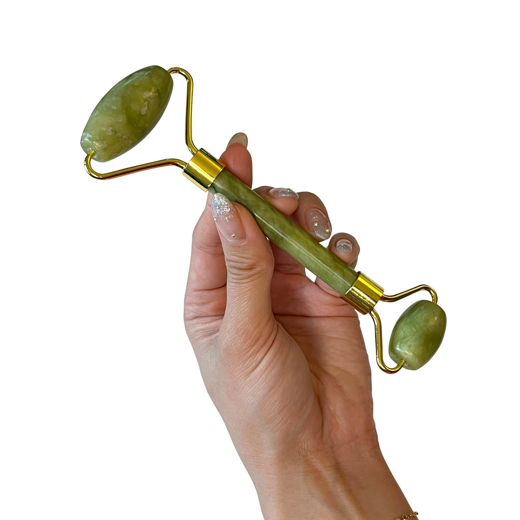 Hand holding a green jade roller with gold accents on a white background