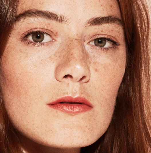 Close-up of a person with freckles and red hair wearing makeup.