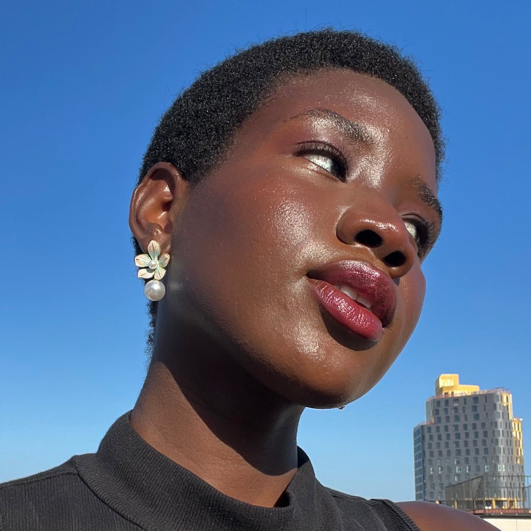 Woman with short hair and earrings against a blue sky with a building in the background