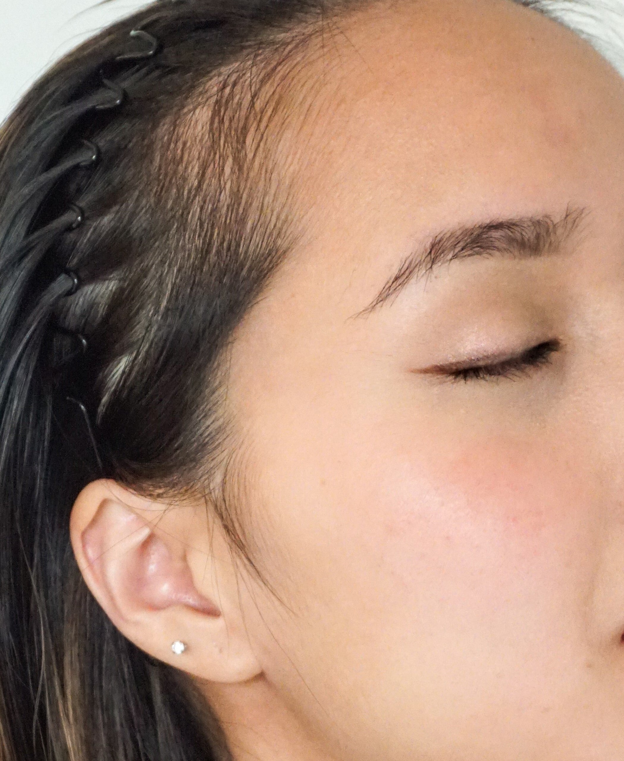 Close-up of a person's face wearing blush with a small earring and braided hair.