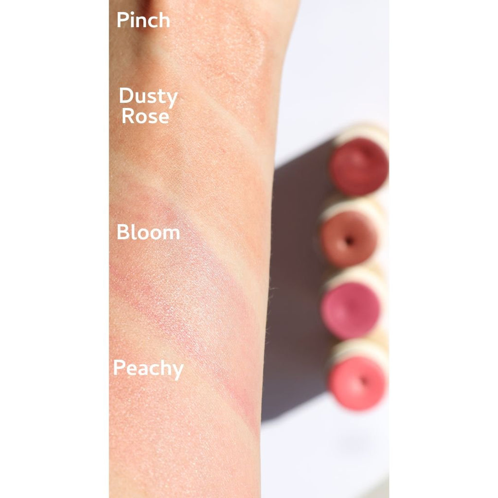 Color swatches on a wrist labeled 'Pinch', 'Dusty Rose', 'Bloom', and 'Peachy' with blush sticks in the same colors.