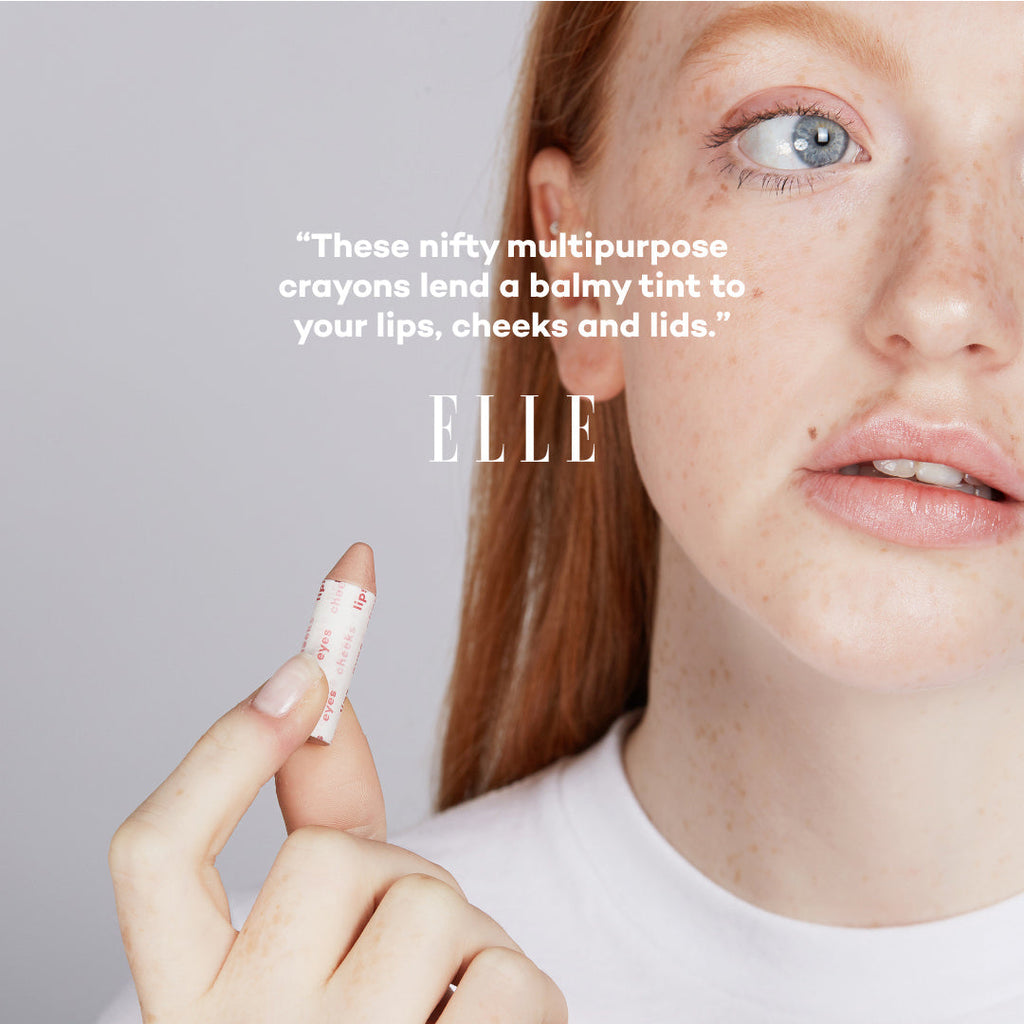 Person holding a makeup crayon with 'ELLE' text on a gray background