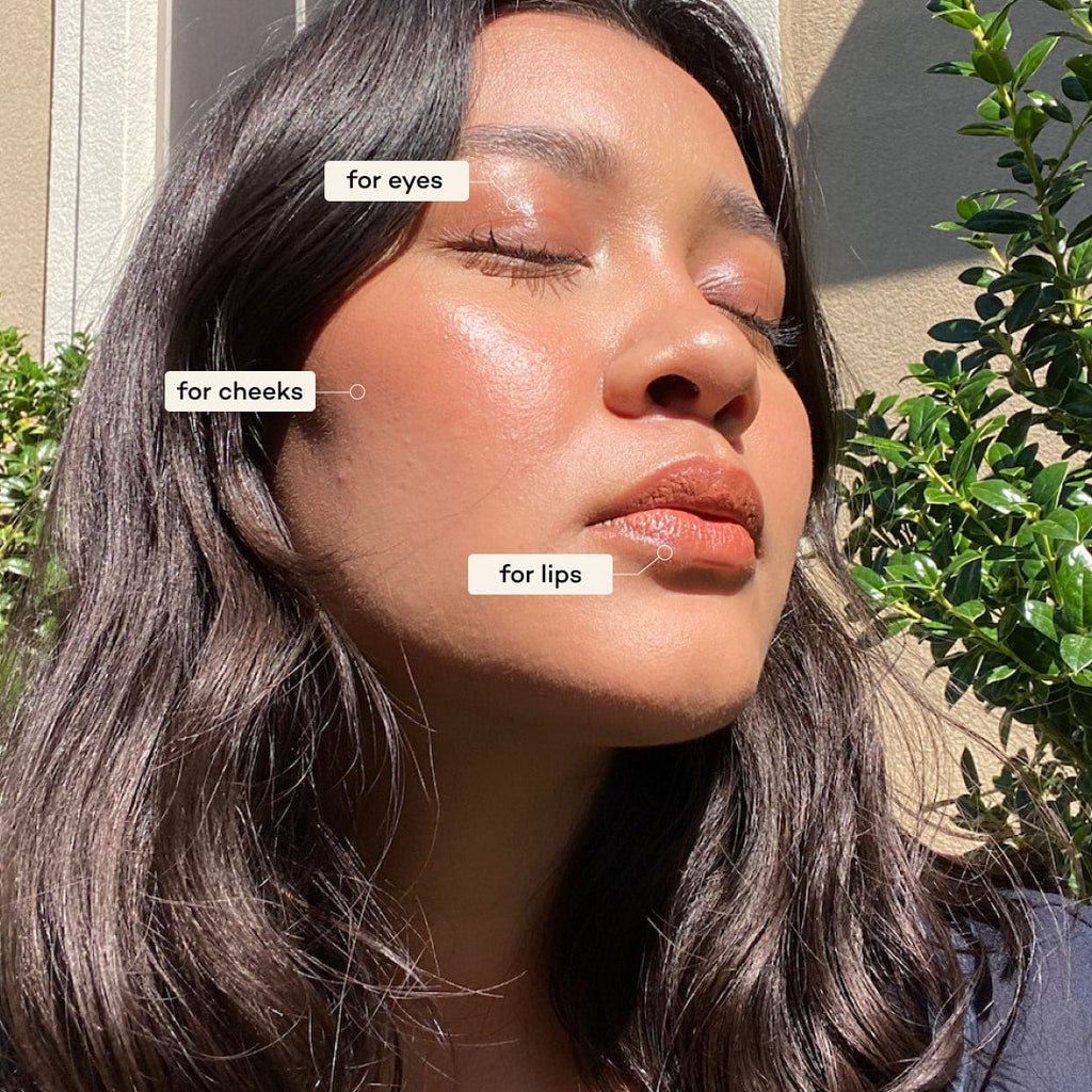 Woman applying makeup with labels for eyes, cheeks, and lips outdoors.