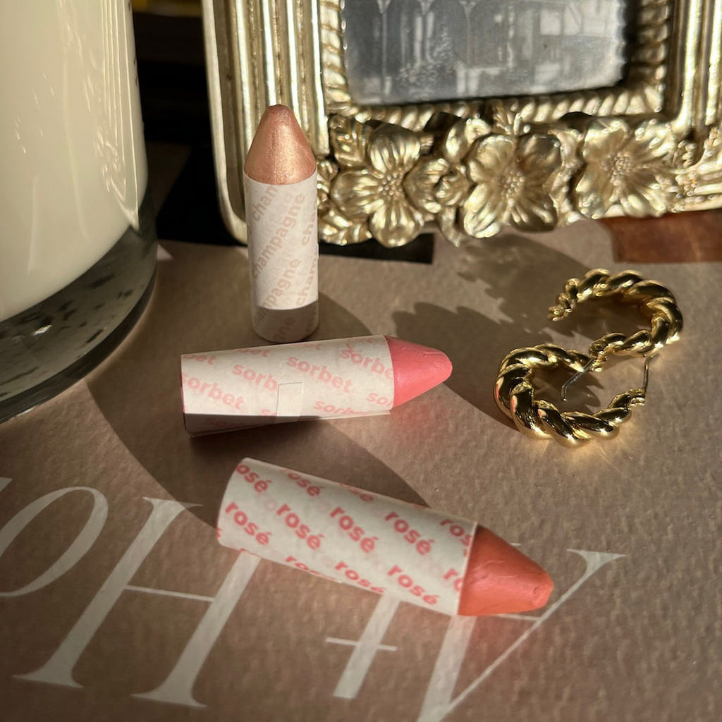 Three lip crayons on a vanity with a decorative mirror in the background.