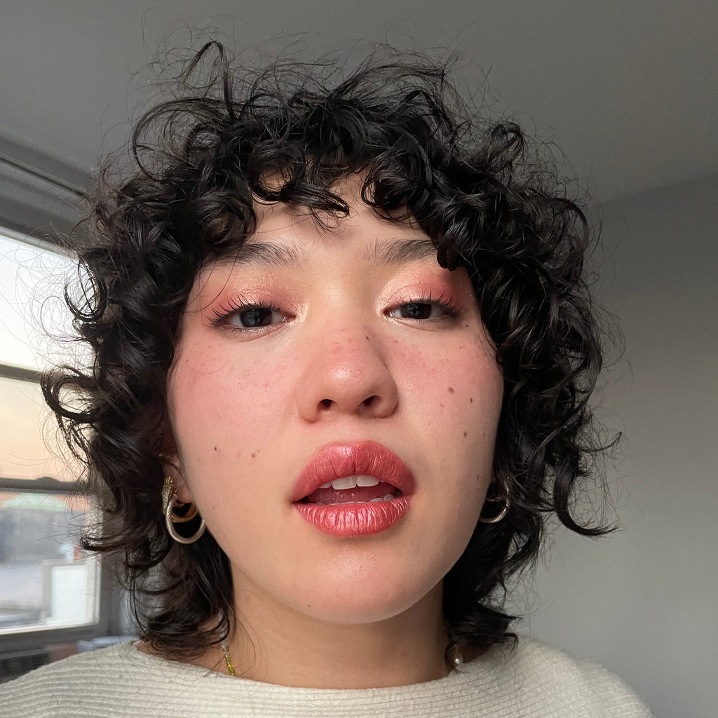 Person with curly hair and pink eyeshadow and lipstick indoors